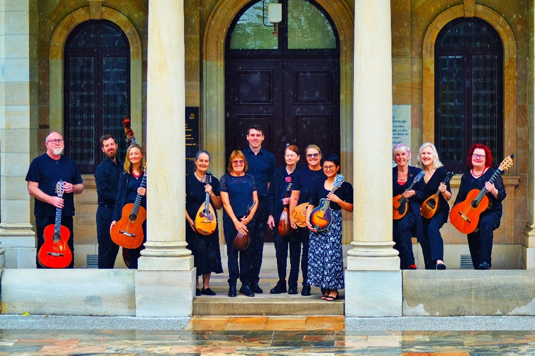 Twelve members of a string ensemble standing in front of a historic building