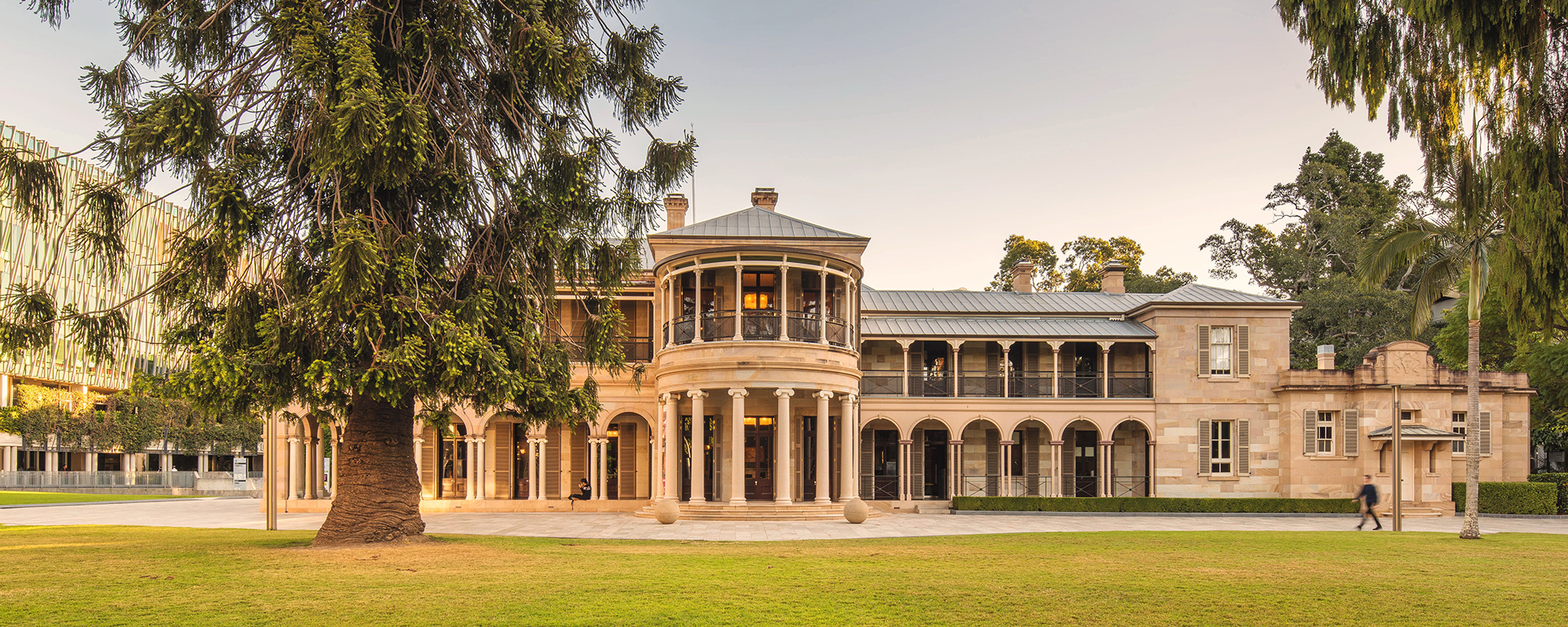 Colonial sandstone building with a large tree and grassed area in the foreground